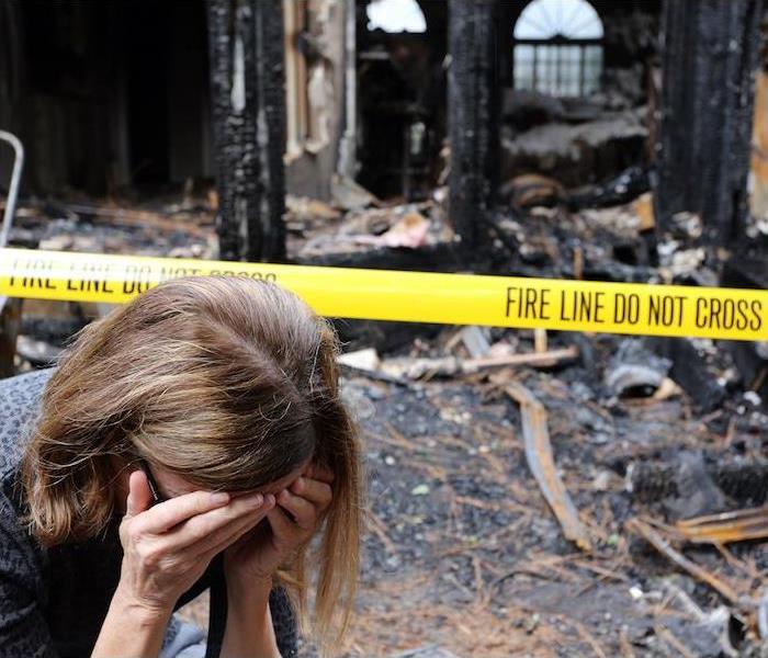 woman with hands covering face upset with burnt house in background 